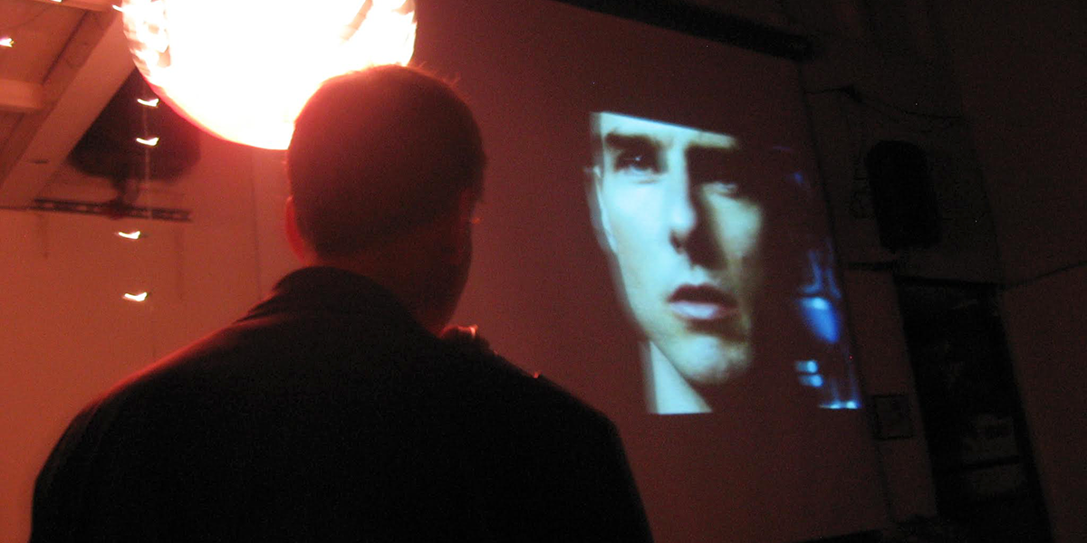 Photo of man's back facing screen projection of actor Tom Cruise